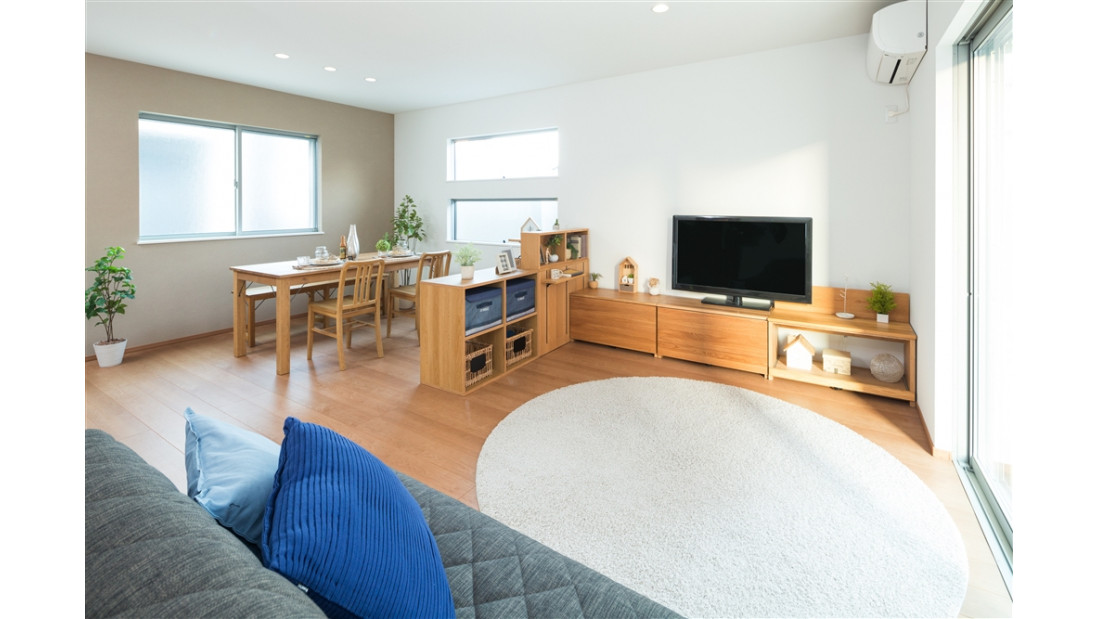 内観はナチュラルスタイル。床色はペール色にアクセントでファブリック調のグレーの壁紙でコーディネート。閉じた外観でありながら陽光が降り注ぐリビングプラン。