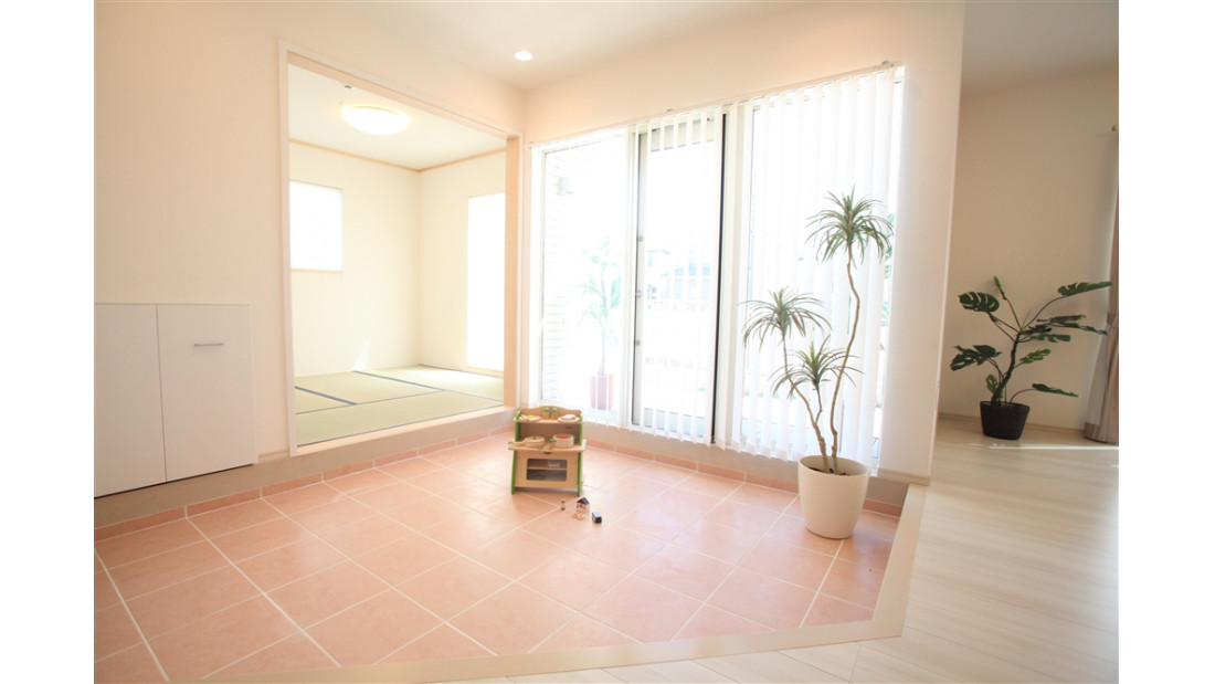 リビング内にタイル貼りのステップダウンフロアを配置。開放的な３枚のガラス窓は、ウッドデッキと繋がっているので、夏は日陰で涼しくプールなどで遊べます。